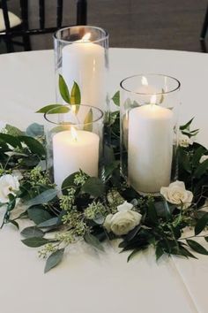 three candles are sitting on a table with flowers and greenery