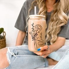 a woman sitting on the floor holding a drink in her hand with flowers painted on it