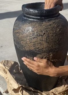 a large black vase sitting on top of a pile of paper next to a person's hand