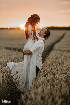 a man and woman are kissing in the middle of a wheat field at sunset or sunrise