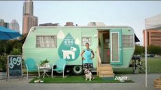 a woman standing in front of a trailer with a dog on the lawn next to it