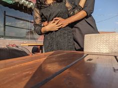 a man and woman standing next to each other on top of a wooden table in front of a building