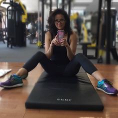 a woman sitting on the ground taking a selfie with her cell phone in a gym