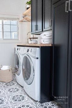 a washer and dryer in a small laundry room with black cabinets, tile flooring and white walls