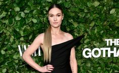 a woman with long hair standing in front of a green wall wearing a black dress