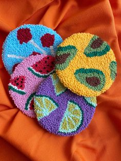 three crocheted coasters with fruit designs on an orange fabric background, one has watermelon and the other has pineapple