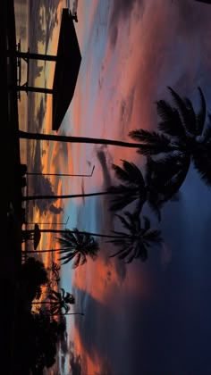 palm trees and umbrellas are silhouetted against an orange, blue, and pink sunset