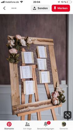 a wooden easel with seating cards on it and flowers hanging from the top,