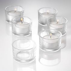 four clear glass votives with lit candles in them on a white surface,