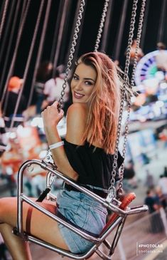 a woman is sitting on a swing at an amusement park and posing for the camera