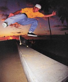 a man riding a skateboard up the side of a cement wall at sunset with palm trees in the background