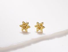 two gold studs on top of a white surface, one with a flower design