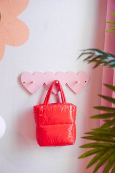 a red purse hanging from the side of a white wall next to a potted plant