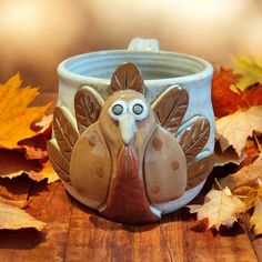 a ceramic turkey mug sitting on top of a wooden table next to leaves and autumn leaves