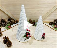 two white christmas trees with red berries and pine cones on the top, surrounded by pine cones