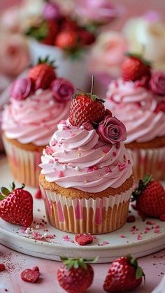 two cupcakes with pink frosting and strawberries on the plate next to them