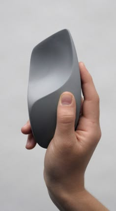 a hand holding a gray object in front of a grey background with no image on it