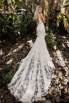 a woman standing in the woods wearing a wedding dress with an open back and long train