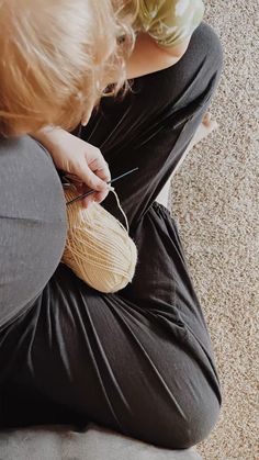 a young child sitting on the floor with a ball of yarn and knitting needles in her hands