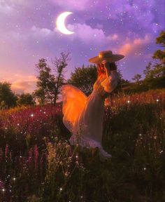 a woman in a dress and hat is standing in the middle of a field at night