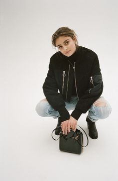 a woman sitting on the floor with her handbag in front of her face and looking at the camera