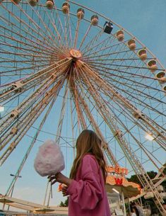 a girl holding cotton candy in front of a ferris wheel