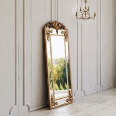 an ornate gold framed mirror against a white wall with a chandelier in the background