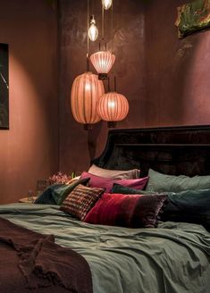 a bed with pillows, blankets and lamps hanging from the ceiling in front of it