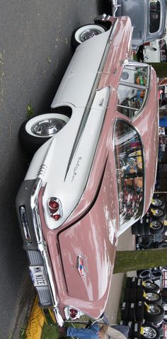 an old pink and white car parked next to other cars