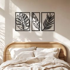 a bed with white linens and two framed tropical leaves on the wall above it