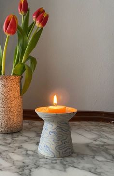 two vases with tulips and a candle on a marble countertop in front of a white wall