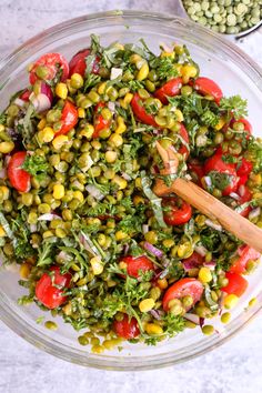 a glass bowl filled with salad and topped with tomatoes, corn, green beans, and parsley