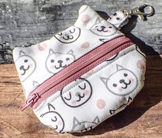 a white coin purse with cats on it sitting on top of a wooden table next to a keychain