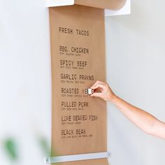 a person holding a piece of paper near a sign on the wall that says fresh tacos