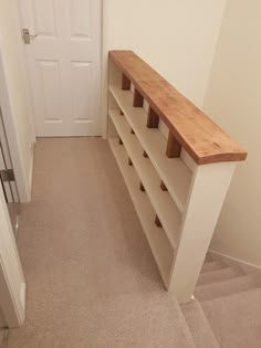 a wooden shelf sitting in the corner of a room next to a white door and carpeted floor