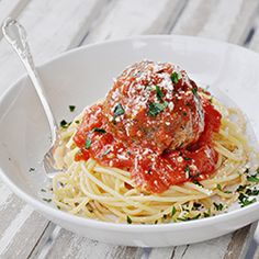 a white bowl filled with spaghetti and meatballs covered in marinara sauce next to a fork