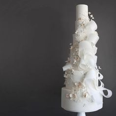 a white wedding cake with flowers and ribbons on it's tiers, in front of a gray background