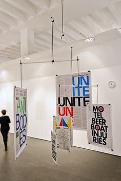 an art gallery with posters hanging from the ceiling and two people walking in front of them