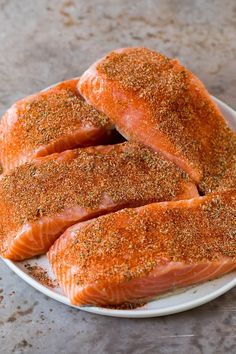 four salmon fillets on a plate with seasoning