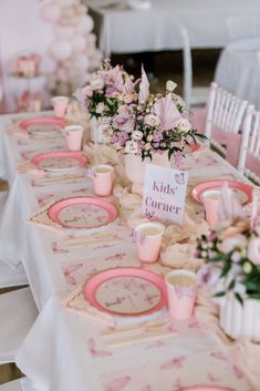 the table is set with pink and white plates, cups and vases on them