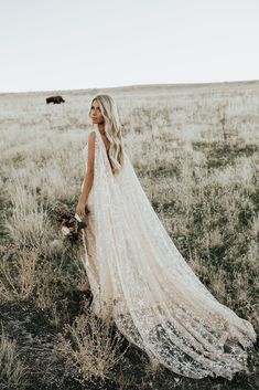 a woman standing in a field wearing a long white dress and holding a flower bouquet