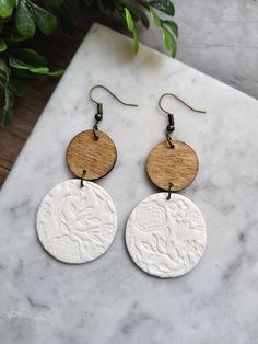 two circular wooden earrings on a marble table next to a potted plant with green leaves