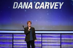 a man holding a microphone while standing in front of a large screen with the words dana carver on it