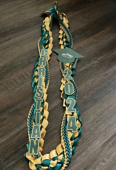 a green and gold graduation ribbon on a wooden floor with a name tag attached to it