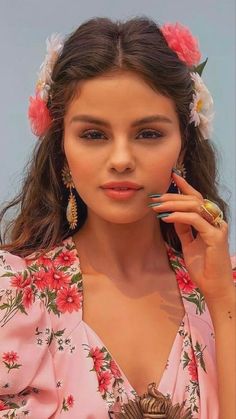 a woman with flowers in her hair holding a cell phone to her ear and looking at the camera