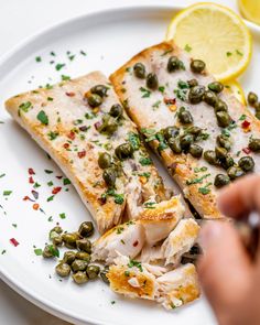 two pieces of fish on a white plate with lemon wedges and green olives