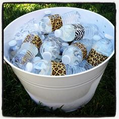 a bucket full of plastic water bottles sitting on the ground in the grass with some animal prints