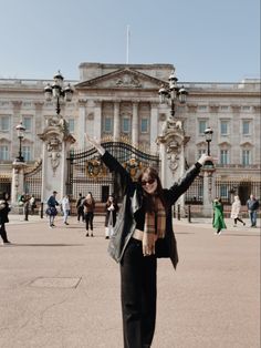 a woman standing in front of a large building with her arms up and hands raised