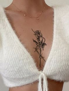 a woman with a rose tattoo on her chest is wearing a white sweater and gold necklace