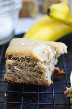 there is a piece of cake with icing on the cooling rack next to some bananas